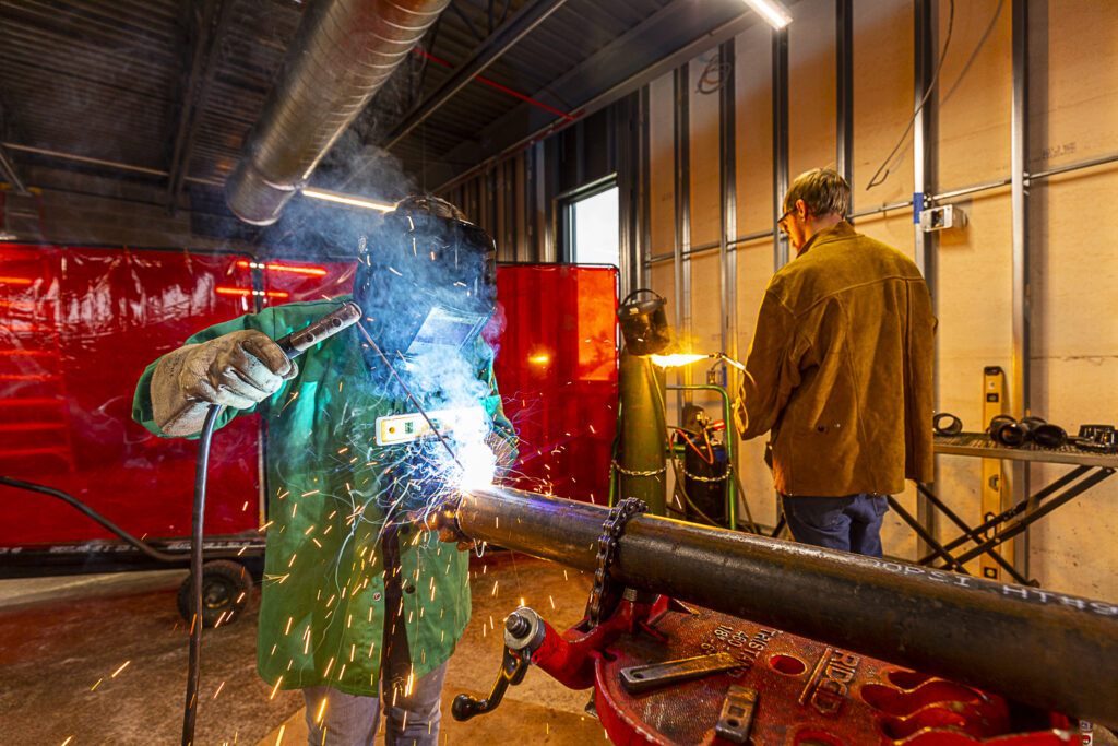 a masked steamfitter welding and a unmasked steamfitter about to weld