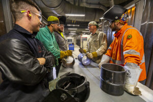 A group of steamfitters talking indoors with pieces of pipes